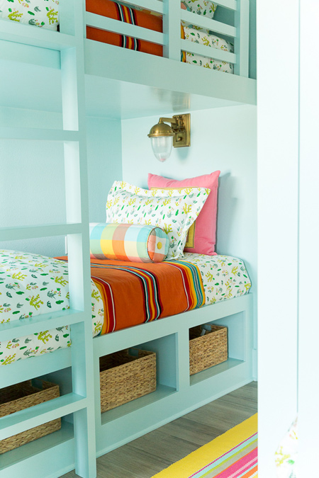 The first bedroom design features four bunk beds spaced along opposing walls. The long, narrow room allows space at the end, between two long windows, for a table and chairs where the children can play. This arrangement is ideal for a smaller home and allows a small play area for younger children.