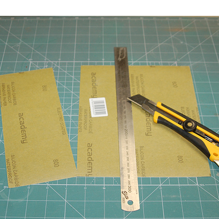 Use a self-healing mat and Olfa cutter to cut regular sandpaper into 3 sanding sheets. Place the sandpaper face down and cut into three sections.
