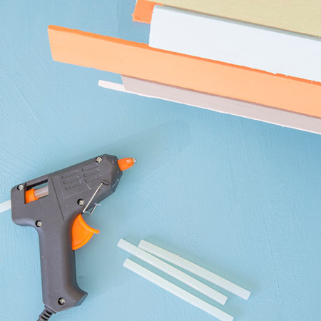 Use a hot glue gun to secure the painted battens onto the wire frame. If you're going for a look that is similar to ours, vary the height and colour of the battens around the frame.