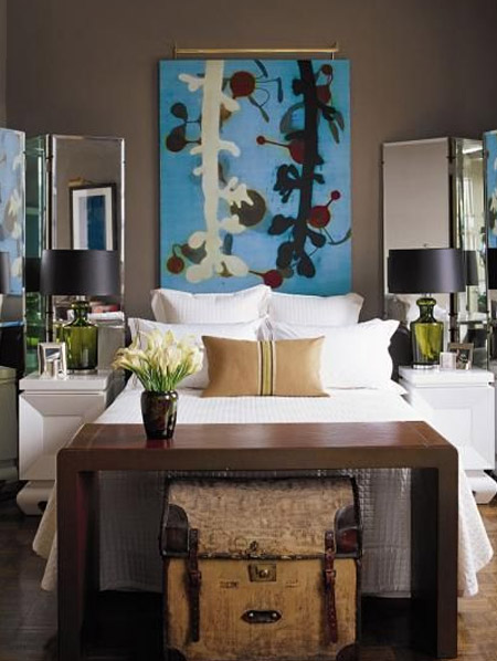 A bold work of art hangs above the bed and immediately draws the eye to the bed. The bed itself is dressed in crisp white bed linens. Large, inviting throw pillows are casually placed to allow the scheme to feel relaxed and informal. Pair these elements with modern or vintage furniture. 